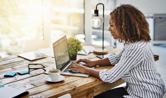 Cropped shot of a woman using her laptop on a wooden table